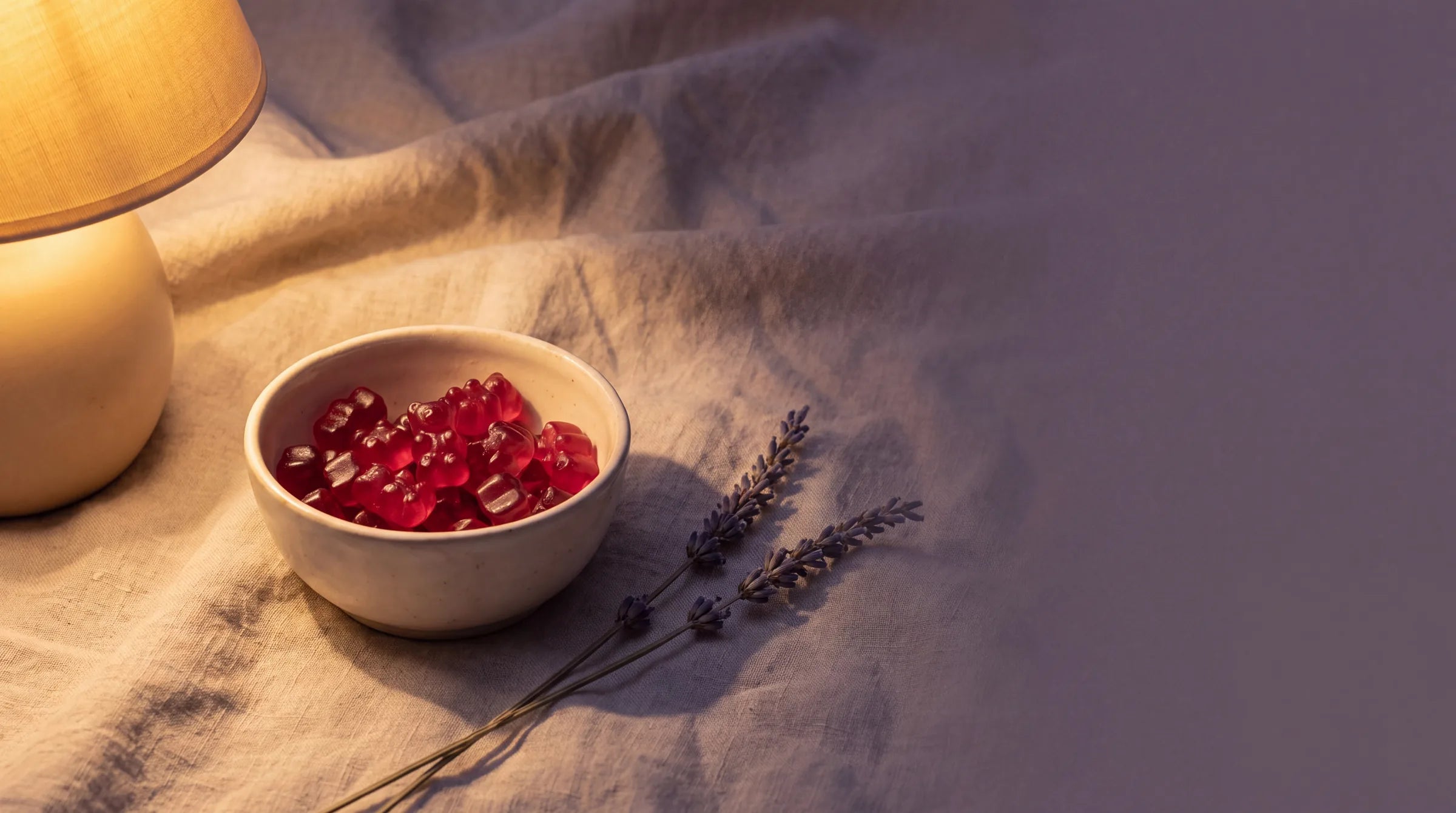 Keramisch schaaltje met rode gummies op linnen naast lavendeltakjes in warm lamplicht