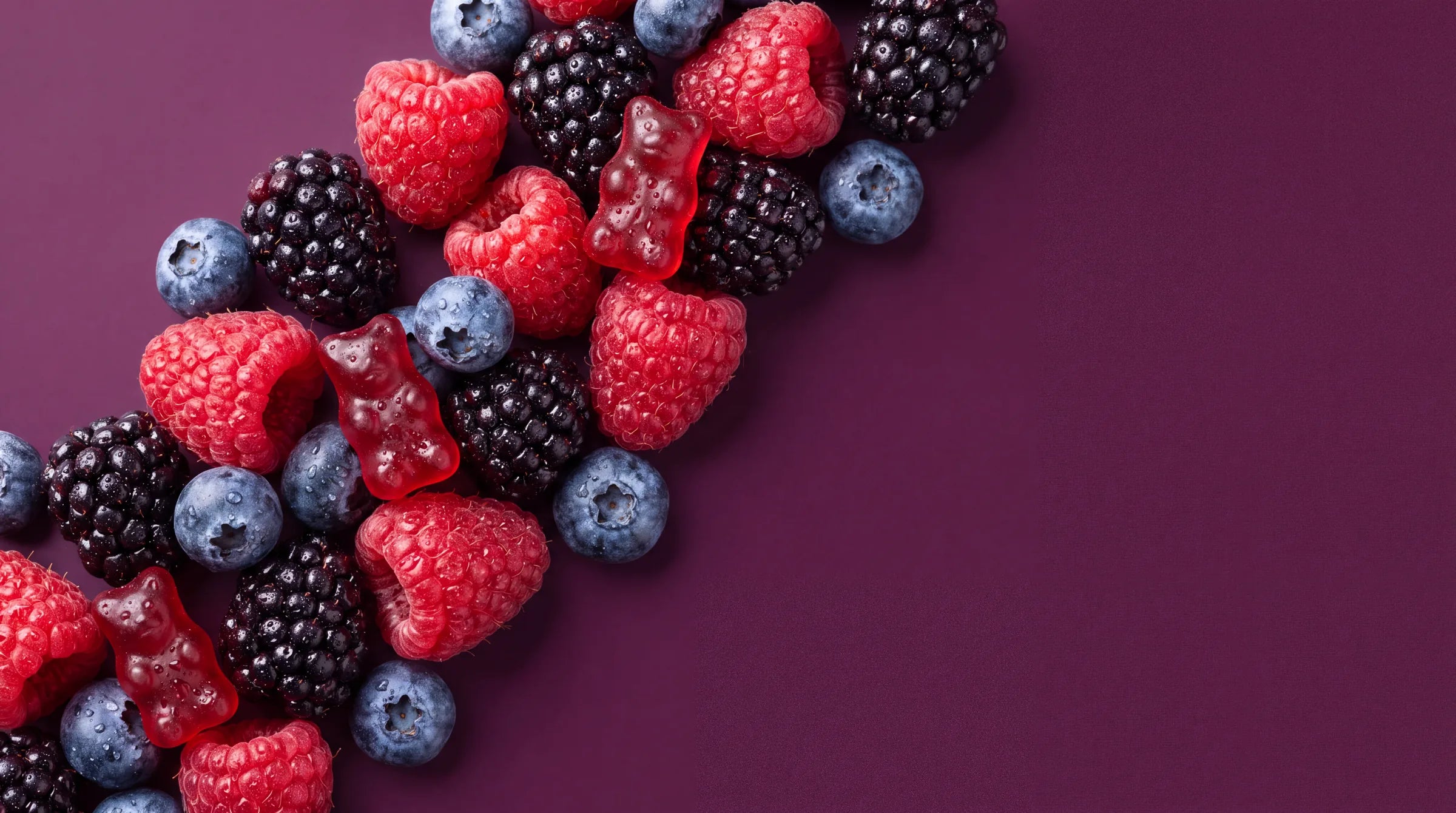 Rode gummies tussen frambozen, bramen en blauwe bessen op pruimkleurig fluweel
