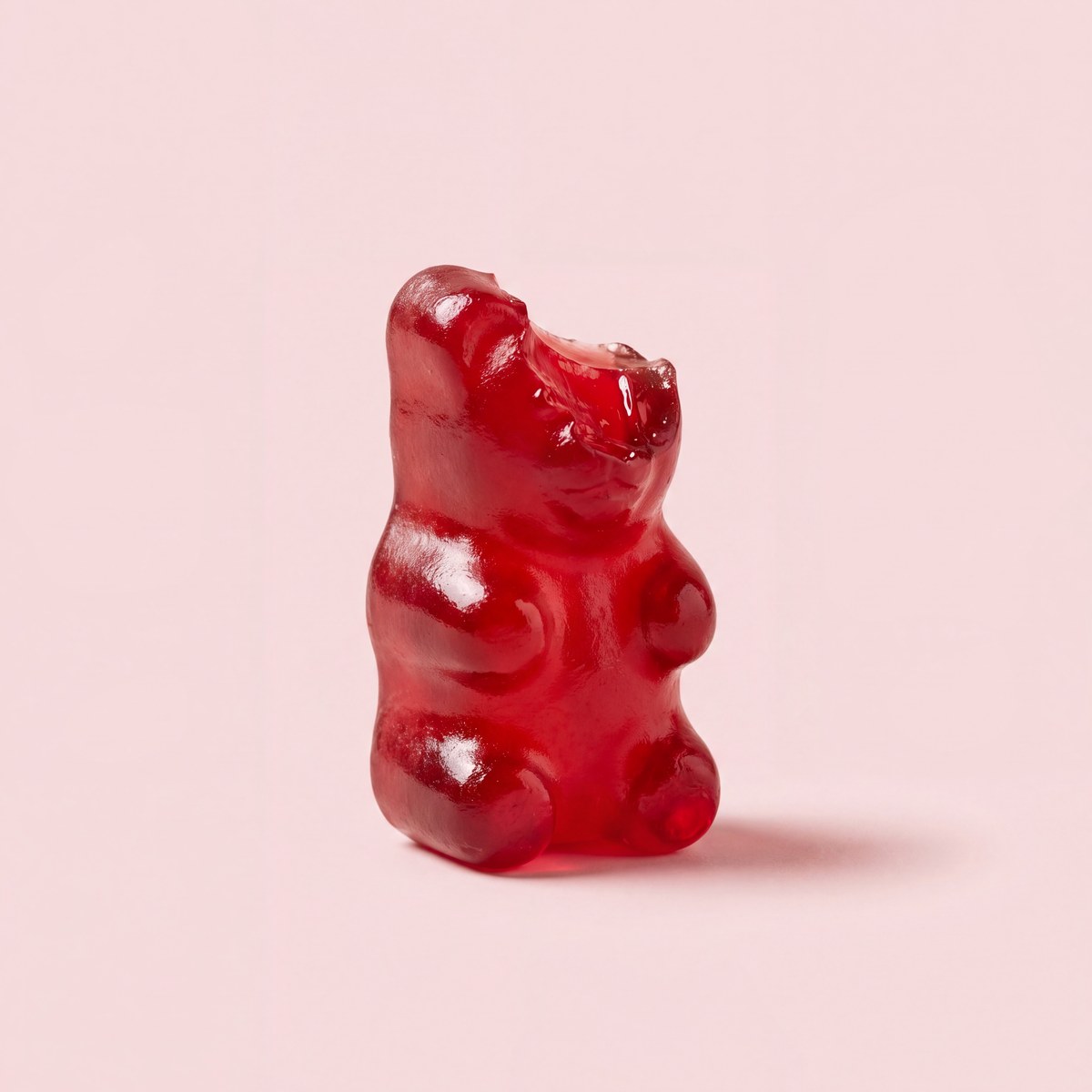 Rood gummybeertje waar een hapje uit is genomen, op zachtroze