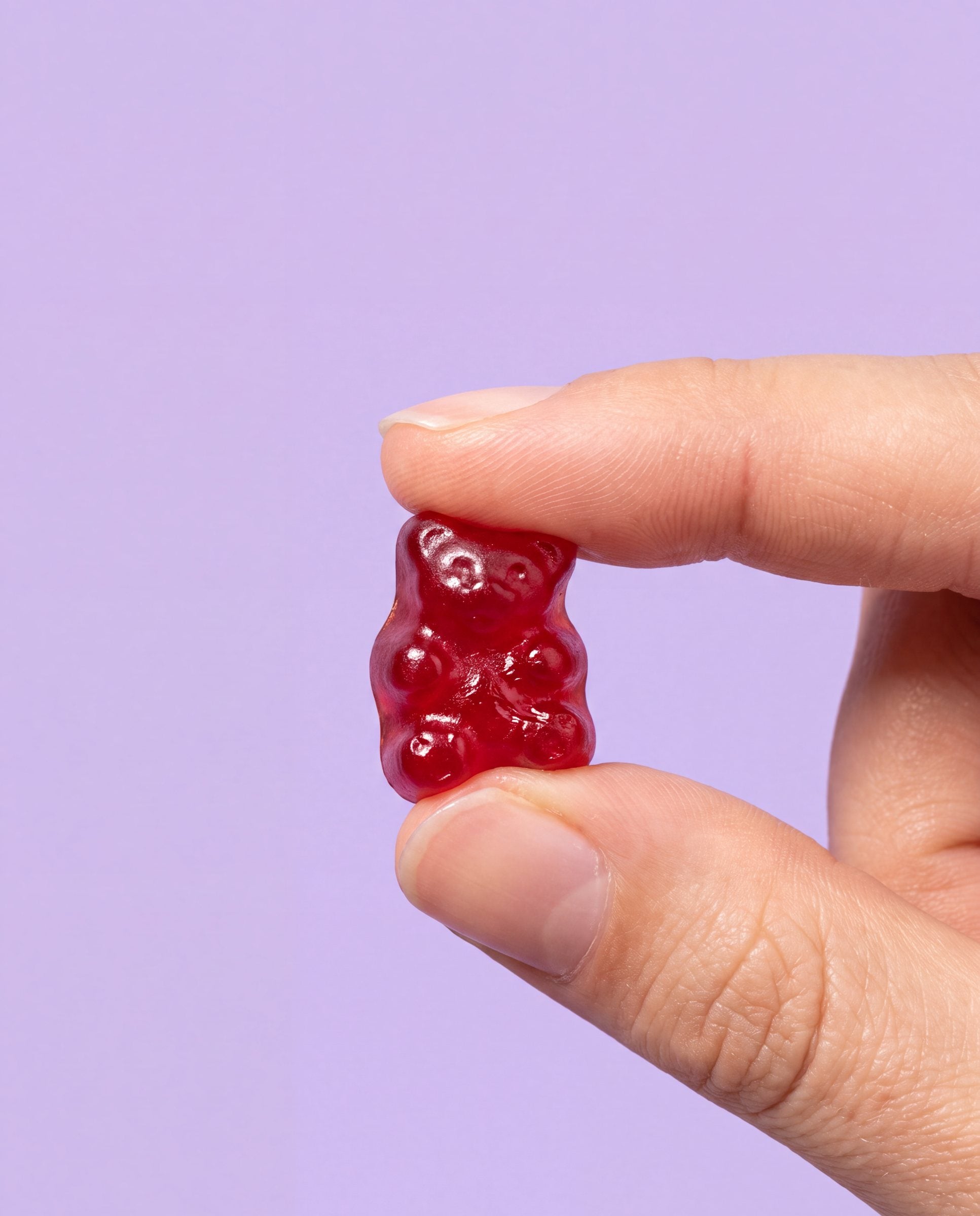 Vingertoppen knijpen zacht in één robijnrood gummybeertje, op pastel lila